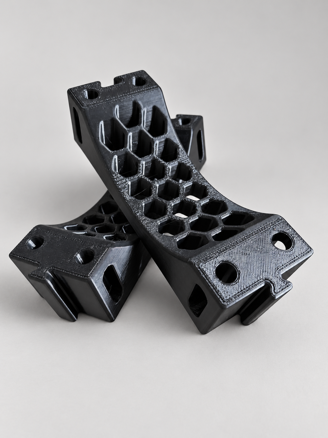 One set of two black ABS scuba tank cradle pieces arranged on a neutral surface, with curved honeycomb supports and linkable connectors. One two-piece set supports one compatible horizontal cylinder.