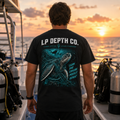 Same Ocean sea turtle artwork on the back of a black LP Depth Co tee, photographed on a dive boat at sunset.