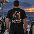 Thumb It. black tee back: scuba-gloved thumbs-up, orange circle, teal bubbles, and No Explanation Required lettering on a dive boat.